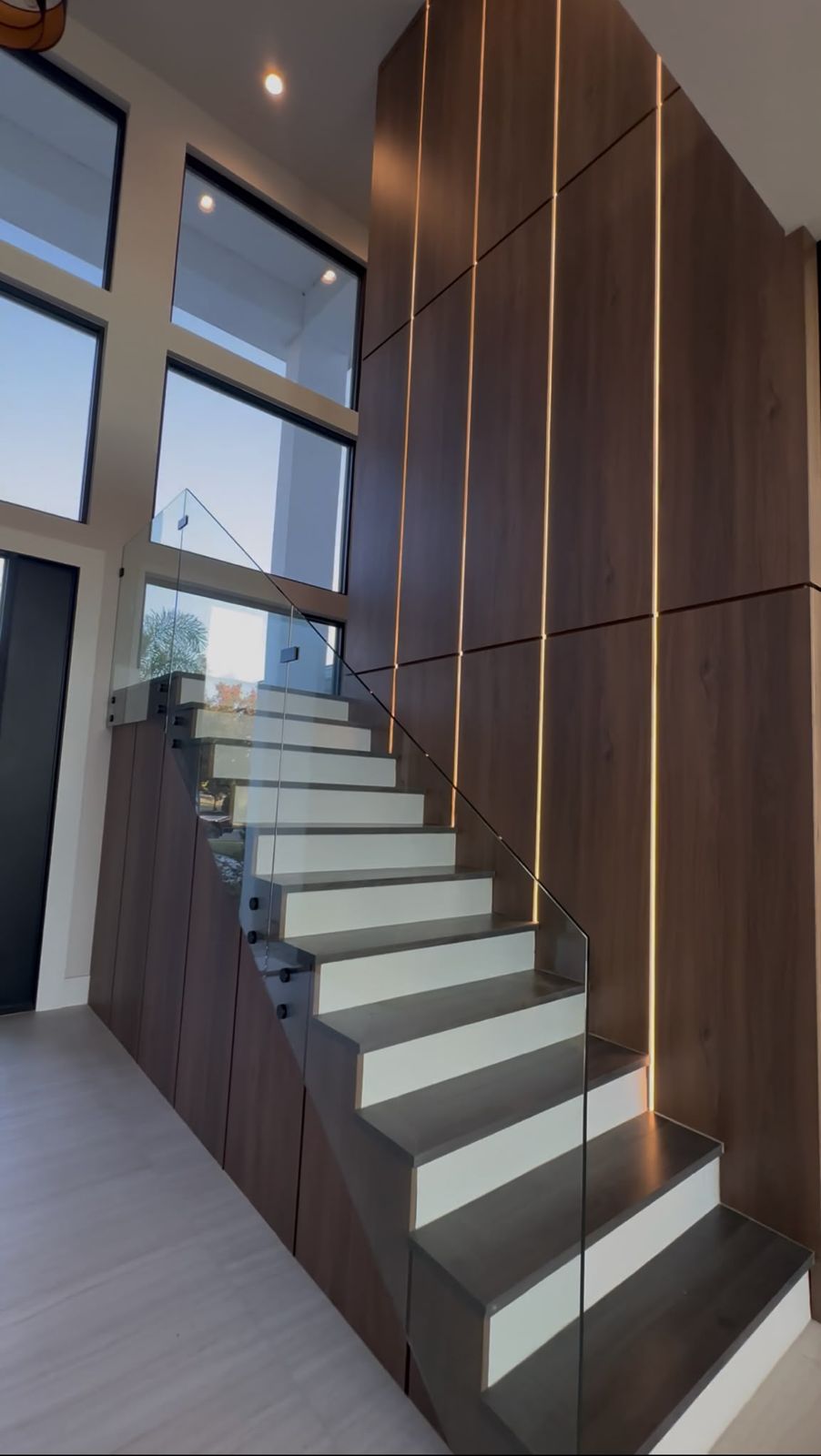 Staircase with wood wall paneling and lit glass treads